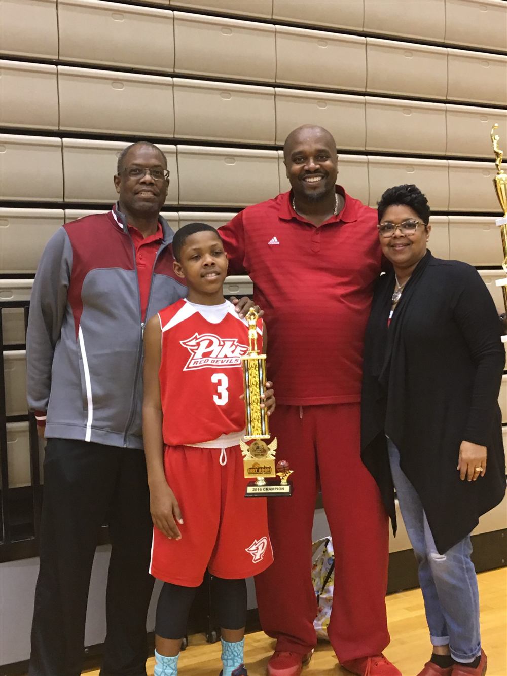 A young We Don't Miss player holding a championship trophy with coaches and family